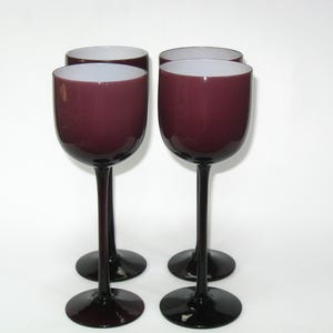 May include: Four wine glasses with a deep purple bowl and a black stem and base. The interior of the bowl is white. The glasses are evenly spaced against a white background.