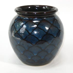 May include: A round, dark blue ceramic vase with a glossy finish. The vase features a textured, scale-like pattern across its surface. The rim is a darker shade of blue, creating a contrast. This decorative vase is suitable for home decor.