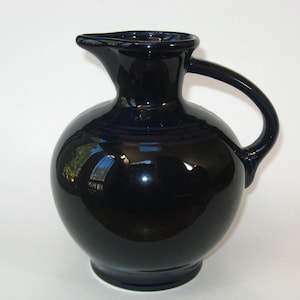 May include: A dark blue ceramic pitcher with a round body and a handle. The pitcher has a glossy finish.