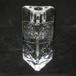 May include: Clear glass candle holder with a rectangular shape and a triangular top. The candle holder has a decorative leaf design etched into the glass. The base of the candle holder is also triangular.