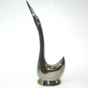 May include: A silver-colored swan figurine with a long, curved neck and a small, round base. The swan's body is smooth and reflective, with a sleek, modern design. This decorative piece is suitable for home decor.