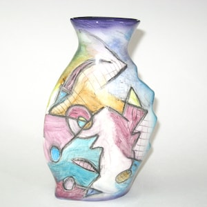 May include: A decorative ceramic vase with a unique, abstract design. The vase features a color palette of blue, purple, yellow, pink, and teal. The design includes geometric shapes and lines, creating a modern and artistic look.