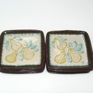 May include: A stack of six square ceramic plates with a brown rim and a white center. The plates feature a hand-painted design of pears with green and blue accents.