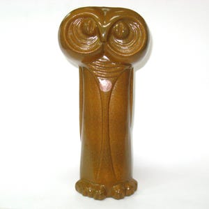 May include: A brown ceramic owl figurine with a detailed design. The owl has large, round eyes and a textured body. The figurine is standing upright and has a detailed base. The owl is a decorative item.