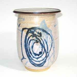 May include: A ceramic vase with a white glaze and blue and black abstract design. The vase has a rounded body and a slightly flared rim.