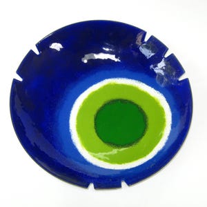 May include: A round, blue decorative bowl with a concentric green and white design in the center. The bowl has a glossy finish and a series of cut-out notches around the rim. The bowl is on a white background.
