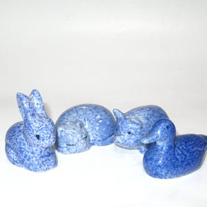 May include: A set of four ceramic animal figurines featuring a rabbit, a curled-up cat, a pig, and a duck. Each piece has a glossy blue and white speckled finish, creating a uniform appearance across the collection of small decorative sculptures.