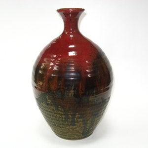 May include: A red and brown ceramic vase with a wide base and a narrow neck. The vase has a glossy finish and a textured surface.