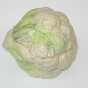 May include: A white cauliflower with green leaves, the cauliflower is split in half and the leaves are folded over the top.