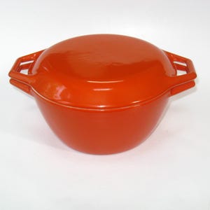 May include: A bright orange enameled cast iron Dutch oven with a matching lid. The round pot features two integrated, open-style handles on opposite sides. The exterior surface is smooth, glossy, and uniform in color, showcasing a rounded base.