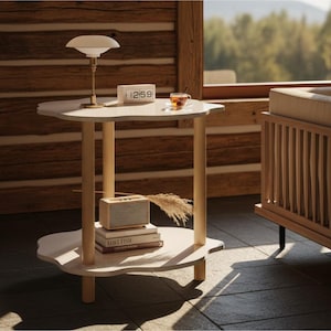 May include: A light-colored, two-tiered side table with a unique, cloud-like shape. The table has a lamp, clock, and a cup on top. A speaker and books are on the lower tier. The table is supported by four cylindrical legs. The room has a wooden wall and a window.