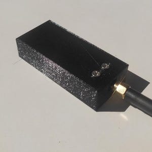 May include: A black rectangular device with a gold-coloured connector and a black antenna. Two small silver-coloured rivets are visible on the top surface. The device is set against a white background.