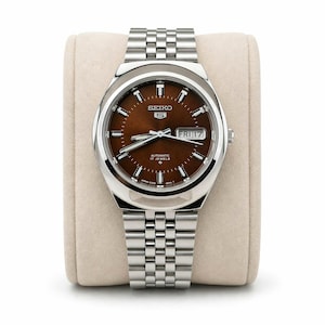 May include: A stainless steel Seiko 5 automatic watch with a brown dial. The watch features a day and date display and a silver-tone bracelet. The watch is displayed on a beige watch pillow.