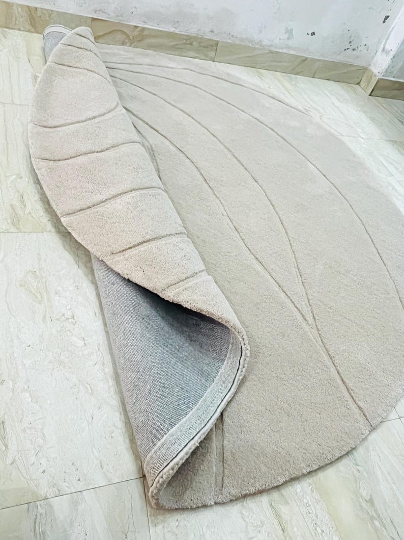 Peut inclure: Tapis beige enroul&eacute; avec un motif incurv&eacute; et textur&eacute;. La surface du tapis pr&eacute;sente des lignes parall&egrave;les en relief, cr&eacute;ant un motif en forme de vagues. Le dessous du tapis est visible, montrant un envers gris.