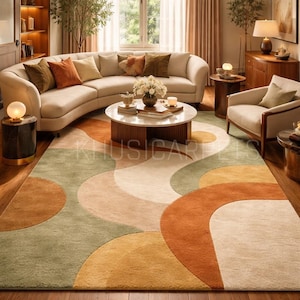 Op de afbeelding: Woonkamer met een grote, gebogen beige bank en een patroonkleed. Het kleed heeft een ontwerp van overlappende cirkels in tinten groen, oranje en beige. Een ronde salontafel staat in het midden. Warme en uitnodigende sfeer.
