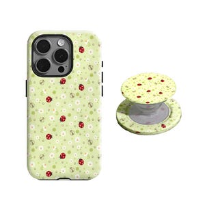 May include: A light green phone case and matching phone grip featuring a repeating pattern of red ladybugs, white daisies, and small green leaves. The phone case has a black camera lens and black side buttons.
