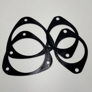 May include: Several black, abstract-shaped gaskets with rounded edges and multiple holes are arranged on a white surface. The gaskets are made of a solid, matte material and appear to be new.