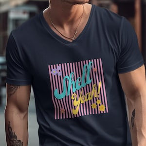 Op de afbeelding: Marineblauwe V-hals T-shirt met een kleurrijke afbeelding. De afbeelding toont de tekst "Shell Yeah!" in turquoise en geel, tegen een roze en wit gestreepte achtergrond met bloemaccenten. Een casual, zomer-thema T-shirt.