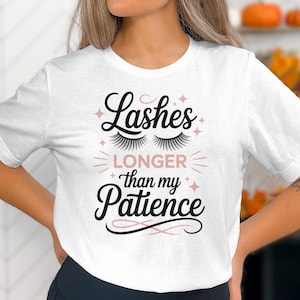 May include: White t-shirt with the text "Lashes Longer than my Patience" in black script and a pair of eyelash illustrations. The text is accented with pink stars and lines. The shirt is a casual, everyday wear item.