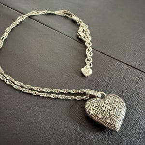 Puede incluir: Collar con colgante de coraz&oacute;n plateado con un dise&ntilde;o tejido y peque&ntilde;as piedras transparentes. El collar tiene una cadena delicada y un peque&ntilde;o dije de coraz&oacute;n cerca del cierre. El colgante mide aproximadamente 2,5 cm de ancho.