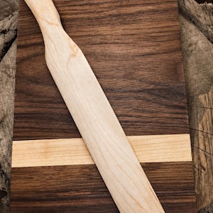 May include: A wooden cutting board with a light-colored wooden spreader. The cutting board is rectangular with a dark brown wood grain, a light wood stripe, and a light-colored wooden spreader.