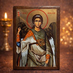 May include: Wooden icon depicting a religious figure with a halo, holding a staff. The figure has wings and wears robes with gold and orange details. The icon has gold lettering and is set against a brown background with a candle.