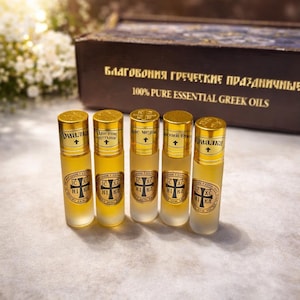 May include: Five small glass bottles with gold lids and labels. The bottles contain a light yellow liquid. The labels feature text in a foreign language and a cross symbol. A wooden box with foreign language text is in the background.