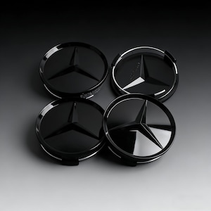 Puede incluir: Cuatro tapacubos negros Mercedes-Benz con acabado brillante. Cada tapacubo presenta el icónico emblema de la estrella de tres puntas en el centro. Los tapacubos están dispuestos sobre un fondo gris degradado.