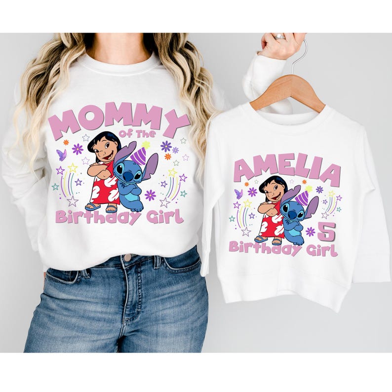 Puede incluir: Sudaderas blancas con gr&aacute;ficos de Lilo y Stitch. Una dice "Mommy of the Birthday Girl", la otra "Amelia 5 Birthday Girl". Los dise&ntilde;os incluyen estrellas y los personajes en un tema de cumplea&ntilde;os.