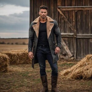 May include: A dark gray long coat with a tan fur collar, worn over a black shirt and dark blue jeans. The person is wearing brown leather boots. The background includes a wooden barn and hay bales in a field.