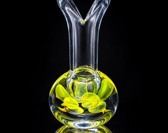 May include: A clear glass vase with a bulbous base containing suspended yellow glass accents. The neck of the vase features a distinct V-shaped opening at the top, creating a flared rim. The design is transparent with bright yellow inclusions.