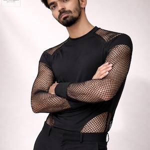 Puede incluir: Camiseta negra de manga larga con detalles de malla en las mangas y los laterales. La camiseta tiene cuello redondo y se combina con pantalones negros. El logotipo de MenPrimeApparel es visible en la esquina superior izquierda.