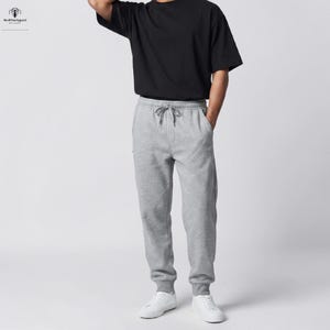 Könnte beinhalten: Ein schwarzes T-Shirt mit kurzen Ärmeln kombiniert mit einer hellgrauen Jogginghose. Die Jogginghose verfügt über einen elastischen Bund mit Kordelzug, Seitentaschen und gerippte Bündchen an den Knöcheln. Das T-Shirt hat einen Rundhalsausschnitt.