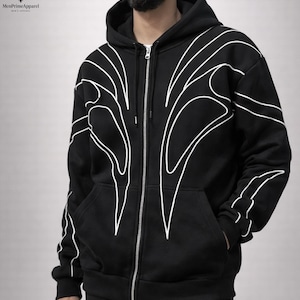 May include: Black zip-up hoodie with white abstract design. The hoodie has a full-length zip, a hood, and front pockets. The white design is on the front, sleeves, and back. Made from a soft, comfortable material.