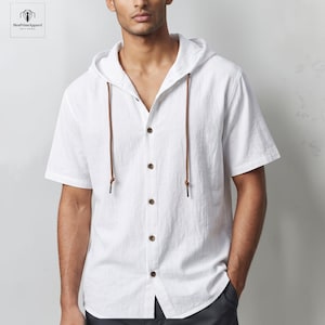 May include: A white short-sleeved button-down shirt featuring a hood with long brown drawstring cords. The shirt has a textured fabric appearance, a classic collar, and five visible brown buttons running down the center front placket.