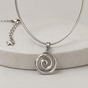May include: A silver-toned necklace featuring a circular spiral pendant. The chain is a smooth snake style, and the necklace includes an adjustable extension chain finished with a small, five-pointed star charm at the end of the clasp mechanism.