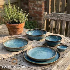 May include: A collection of handmade ceramic bowls and plates with a turquoise glaze and brown rims. The set includes various sizes, from small bowls to large plates, arranged on a wooden table. A potted plant is in the background. The text "SOL CERAMIC ART" is visible.