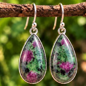 May include: A pair of teardrop-shaped earrings featuring polished ruby zoisite stones with vibrant magenta and deep green inclusions, set in smooth silver-toned metal frames with matching silver-toned shepherd hook ear wires for hanging.