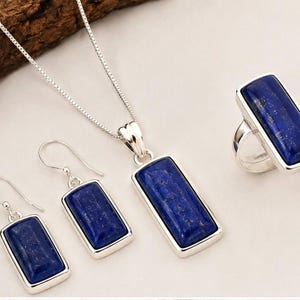 Puede incluir: Un conjunto de joyería que consta de un collar de plata con un colgante rectangular de lapislázuli, un par de pendientes colgantes rectangulares a juego con ganchos de plata y un anillo de plata con una piedra rectangular de lapislázuli.