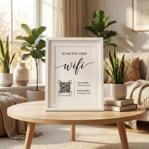 May include: A framed white sign on a wooden table displays the word "wifi" in elegant script, along with a QR code and text that reads "Scan the code" and "Scan to connect". The sign is surrounded by plants and books.