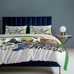 Könnte beinhalten: Weißes Bettwäsche-Set mit einem Design zum Thema Natur, einschließlich eines Vulkans, eines Flusses und eines Sonnenuntergangs. Das Set zeigt den Text "WINGS UP STRONG" und "MADE BY GOD" auf den Kissenbezügen und dem Bettbezug. Der Bettbezug trägt auch den Text "THOSE WHO HOPE IN THE LORD WILL RENEW THEIR STRENGTH ISAIAH 40:31".
