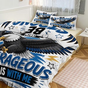 Könnte beinhalten: Weißes Bettwäsche-Set mit einer Grafik eines Weißkopfseeadlers in Blau und Schwarz. Bettdecke und Kissenbezüge zeigen den Text "BE STRONG AND COURAGEOUS, GOD IS WITH ME". Das Design beinhaltet Sterne und Blitze.
