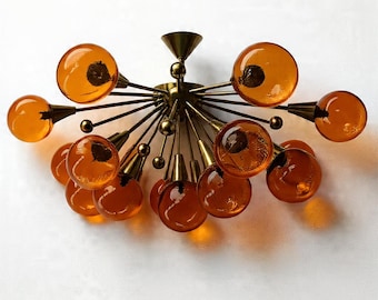 May include: A mid-century modern ceiling light fixture with a brass finish and amber glass globes. The light has multiple arms extending from a central point, each holding a round glass globe. The globes are a warm orange color.