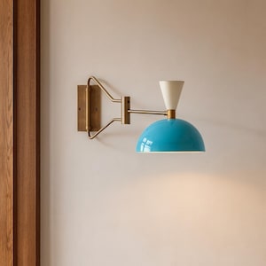 May include: A wall-mounted light fixture with a brass finish and a turquoise dome-shaped shade. The fixture has a white cone-shaped element and a brass arm extending from a rectangular base. The light is mounted on a light-colored wall.