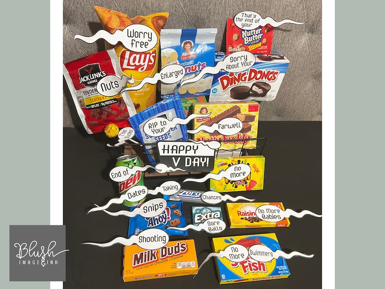 May include: A black wire basket filled with a variety of snack foods, including crisps, sweets, biscuits, and crackers. The basket is decorated with humorous signs that say "Worry Free", "Sorry About Your Ding Dongs", "Happy V Day!" and more.