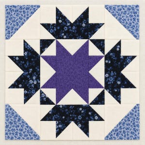 May include: A square quilt block featuring a central purple star surrounded by four dark navy blue floral star points. The corners are accented with light blue floral fabric, and the background consists of solid cream-colored fabric.