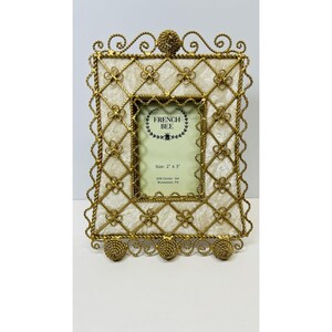 May include: A rectangular picture frame featuring a gold-toned wire lattice overlay with small flower accents on a cream-colored fabric background. The center insert displays the text FRENCH BEE and Size: 2" x 3" with additional copyright details.