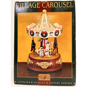 May include: A Village Carousel toy in a box with the text Village Carousel and Maisto. The carousel features a gold roof, white trim with green wreaths and gold bells, and horses in black and white on a round, dark red base with gold accents.