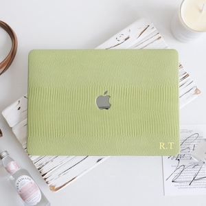 May include: A light green laptop skin with a textured lizard-skin pattern and a central cutout for an Apple logo. The bottom right corner features the gold-colored initials R.T. printed in a serif font on the matte, reptile-embossed surface.