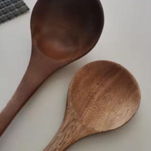 May include: Two wooden spoons with long handles and rounded bowls. One spoon is a dark brown color, while the other is a lighter, natural wood tone. The spoons are likely for cooking or serving.